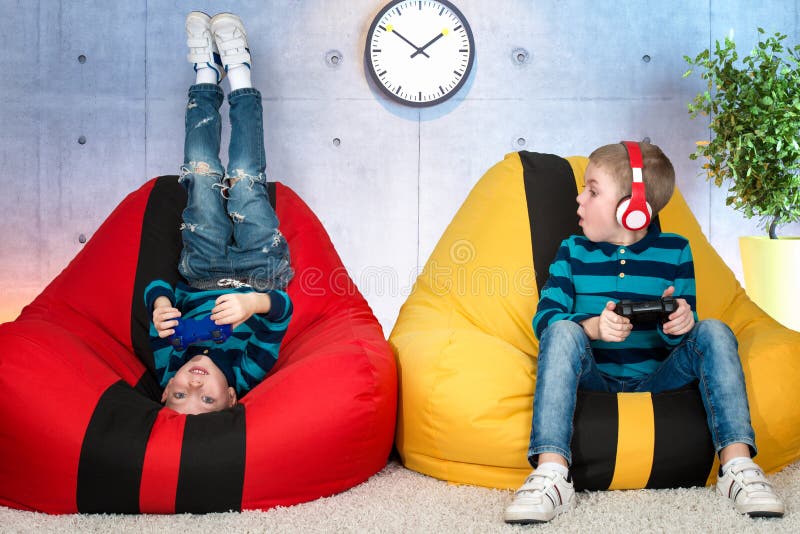 Les enfants s'asseyent sur des sacs de chaises et des jeux vidéo de jeu Émotions du ` s d'enfants photos stock Les enfants s'asseyent sur des sacs de chaises et des jeux vidéo de jeu Émotions du ` s d'enfants photos stock