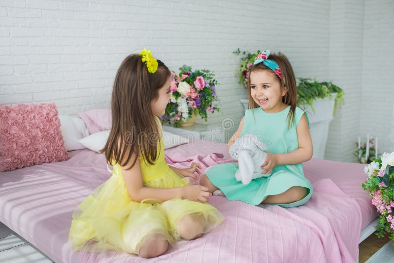 Les filles assez petites dans un jaune et des robes de turquoise jouent sur un lit dans un studio images libres de droits Les filles assez petites dans un jaune et des robes de turquoise jouent sur un lit dans un studio images libres de droits