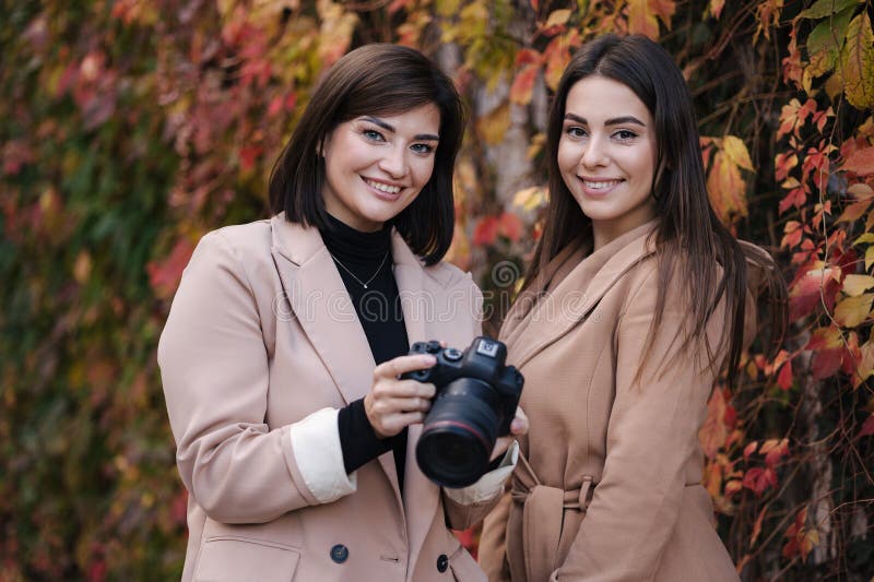 Les filles passent en revue les photos qu'elles ont prises sur la caméra. deux belles femmes devant des arbres rouges et jaunes. images stock