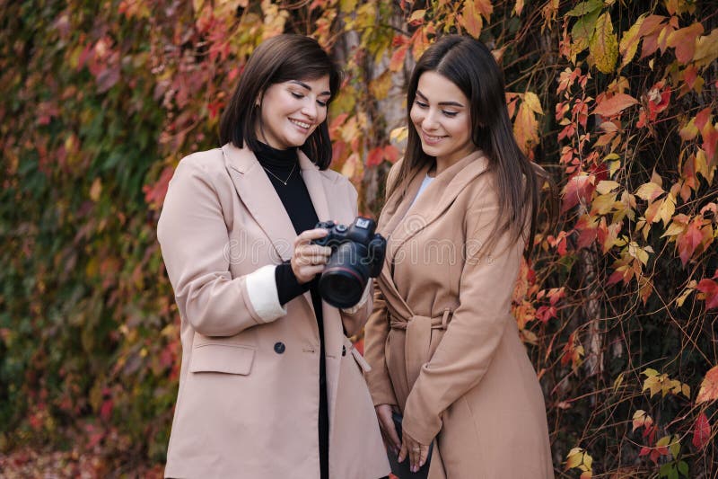 Les filles passent en revue les photos qu'elles ont prises sur la caméra. deux belles femmes devant des arbres rouges et jaunes. images stock