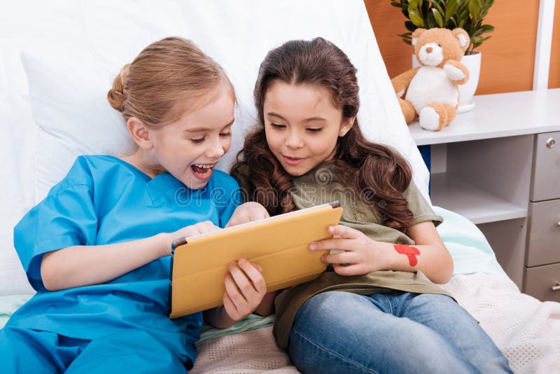 Les filles soignent et patient à l'aide du comprimé numérique tout en se trouvant sur le lit d'hôpital photographie stock Les filles soignent et patient à l'aide du comprimé numérique tout en se trouvant sur le lit d'hôpital photographie stock