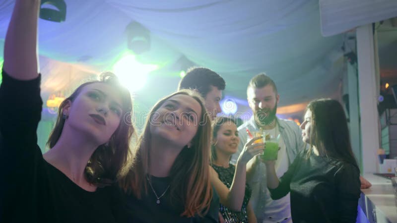 Les filles à la mode à la boîte de nuit fait la photo de selfie au téléphone portable sur le fond des lumières de disco derrière