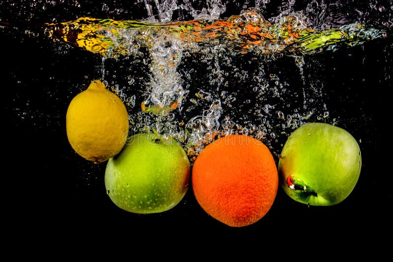 Les fruits flottent dans l'eau avec des bulles, le fruit est dans l'éclaboussure de l'eau et est isolé sur un fond noir photos stock Les fruits flottent dans l'eau avec des bulles, le fruit est dans l'éclaboussure de l'eau et est isolé sur un fond noir photos stock