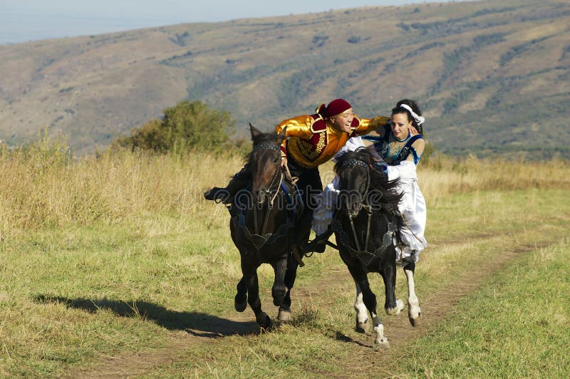 Les gens dans des robes nationales montent à cheval à la campagne, vers Almaty, Kazakhstan photographie stock Les gens dans des robes nationales montent à cheval à la campagne, vers Almaty, Kazakhstan photographie stock
