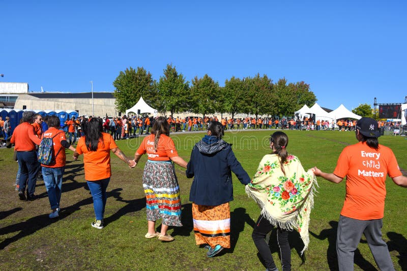 Ottawa, Canada - September 30, 2022: People hold hands in a large circle for a round dance as drummers perform on stage at event at LeBreton Flats on National Day for Truth and Reconciliation Day which is a statutory holiday in Canada. Ottawa, Canada - September 30, 2022: People hold hands in a large circle for a round dance as drummers perform on stage at event at LeBreton Flats on National Day for Truth and Reconciliation Day which is a statutory holiday in Canada