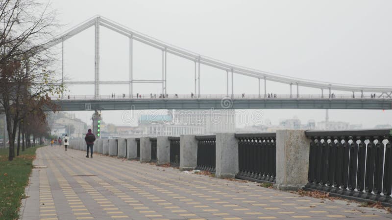 Les gens marchent sur le quai de la ville le long de la rivière dans le brouillard avec le pont et la partie industrielle de la v