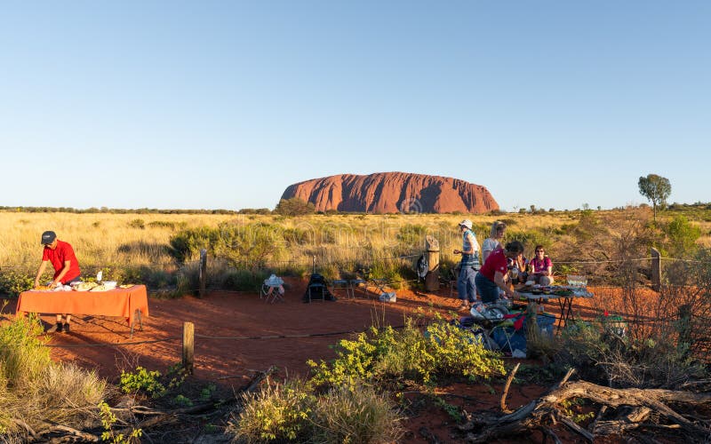 Les gens mettant des tables de buffet de BBQ de dîner au point de vue de coucher du soleil d'Uluru et à la roche d'Ayers à l'arri image libre de droits Les gens mettant des tables de buffet de BBQ de dîner au point de vue de coucher du soleil d'Uluru et à la roche d'Ayers à l'arri image libre de droits