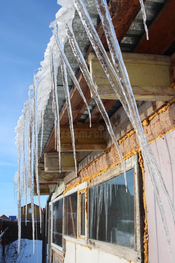 Les glaçons de fonte de ressort accrochent du toit la maison en mars photographie stock Les glaçons de fonte de ressort accrochent du toit la maison en mars photographie stock