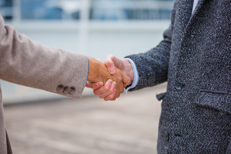 Les hommes d'affaires dans un manteau sur le pilier se serrent la main image libre de droits Les hommes d'affaires dans un manteau sur le pilier se serrent la main image libre de droits