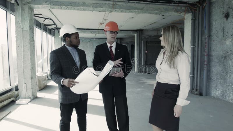 Les hommes, la femme dans le costume et le casque discutent le modèle, communiquent avec l'acheteur Constructeur d'ingénieur en c
