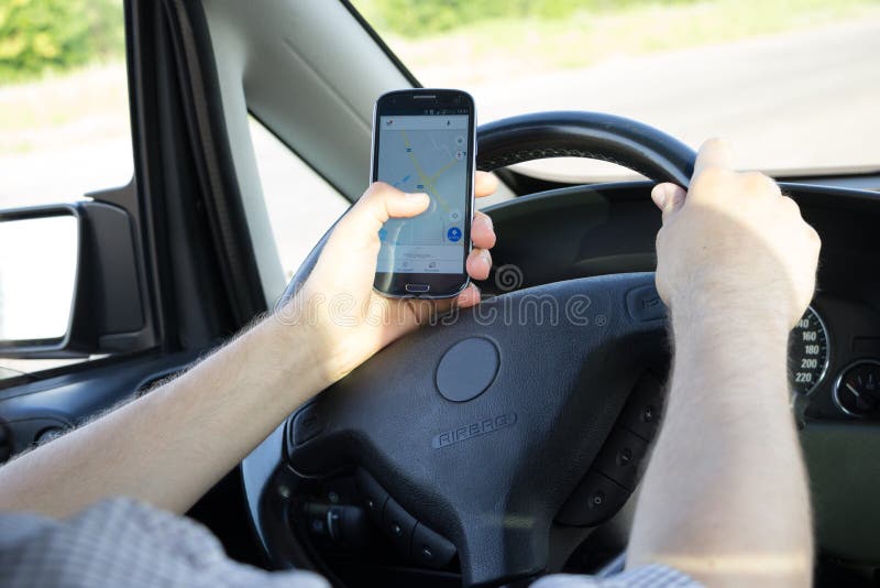 Les hommes tiennent une main sur le volant et rechercher un itinéraire sur le navigateur dans le smartphone par l'autre main photographie stock libre de droits Les hommes tiennent une main sur le volant et rechercher un itinéraire sur le navigateur dans le smartphone par l'autre main photographie stock libre de droits