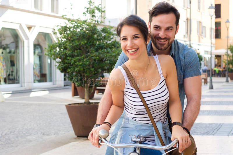 Les jeunes amants couplent monter une bicyclette dans la rue image stock Les jeunes amants couplent monter une bicyclette dans la rue image stock