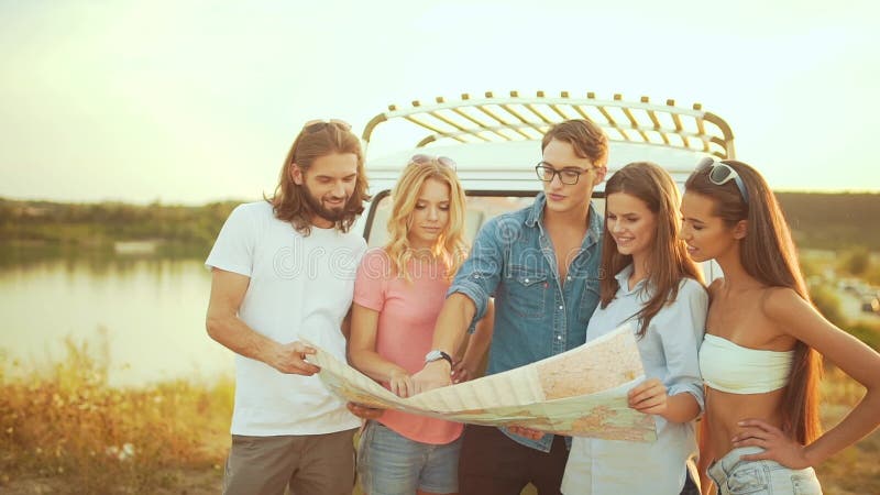 Les jeunes avec la carte près de la voiture en été. Groupe d'amis de sourire heureux. banque de vidéos