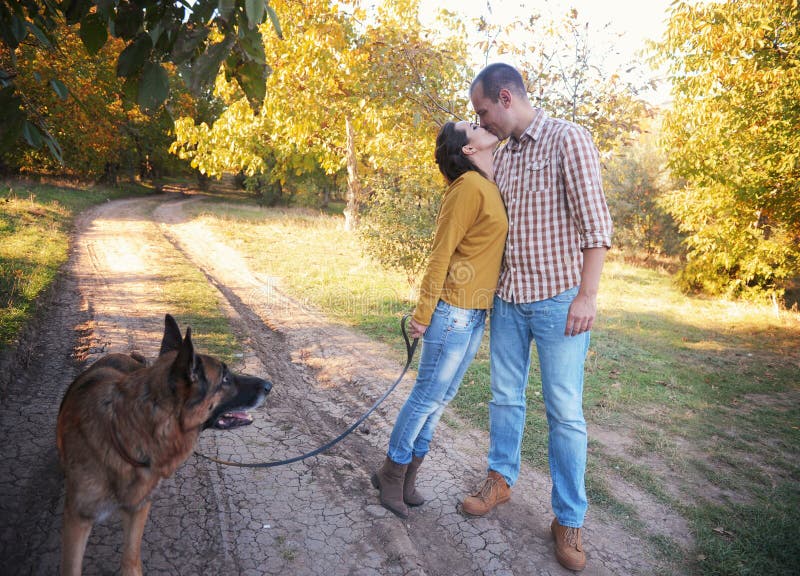 Les jeunes couples d'amour marchant en parc avec leur chien de berger allemand, ont un baiser photo libre de droits Les jeunes couples d'amour marchant en parc avec leur chien de berger allemand, ont un baiser photo libre de droits