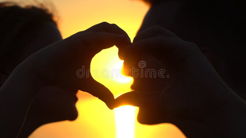 Les jeunes couples heureux faisant le coeur forment avec des mains à l'océan au coucher du soleil Silhouette de l'homme et de fem banque de vidéos