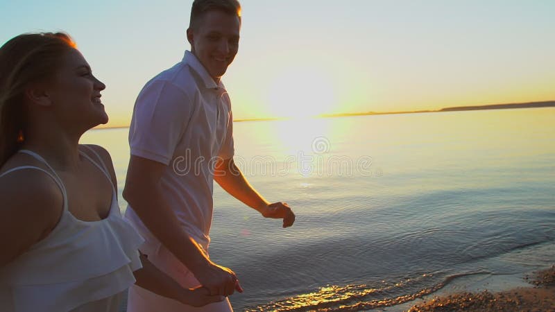 Les jeunes couples heureux jouant avec un cerf-volant sur la mer échouent au coucher du soleil Homme et femme appréciant le temps banque de vidéos
