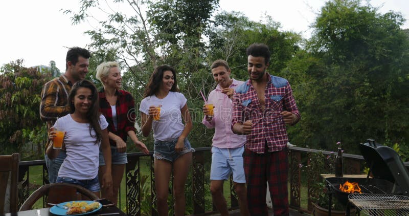 Les jeunes dansant tandis qu'homme latin faisant cuire le rassemblement gai de groupe d'amis de barbecue sur la terrasse d'été ay banque de vidéos