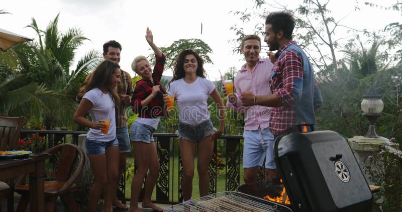 Les jeunes dansant tout en faisant cuire le rassemblement gai de groupe heureux de barbecue sur la terrasse d'été ayant la partie banque de vidéos