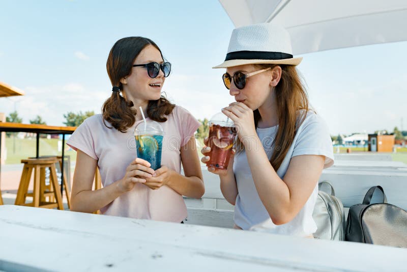 Les jeunes filles de l'adolescence de sourire boivent les boissons régénératrices fraîches d'été un jour ensoleillé chaud en café photographie stock Les jeunes filles de l'adolescence de sourire boivent les boissons régénératrices fraîches d'été un jour ensoleillé chaud en café photographie stock