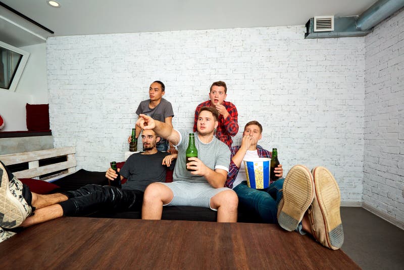 Les jeunes garçon-fans regardent la TV, détendent, ont l'amusement et boivent de la bière ami photo libre de droits Les jeunes garçon-fans regardent la TV, détendent, ont l'amusement et boivent de la bière ami photo libre de droits