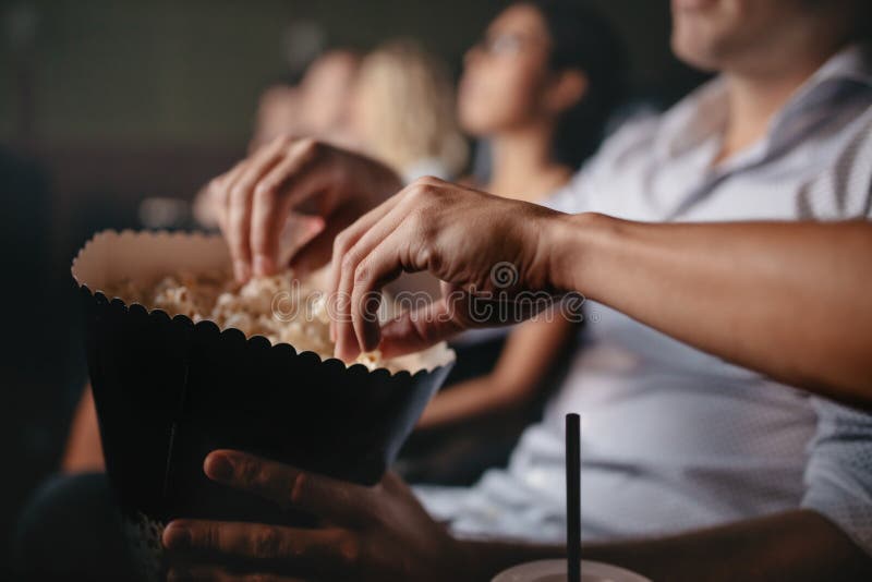 Close up shot of young people eating popcorn in movie theater, focus on hands. Close up shot of young people eating popcorn in movie theater, focus on hands.