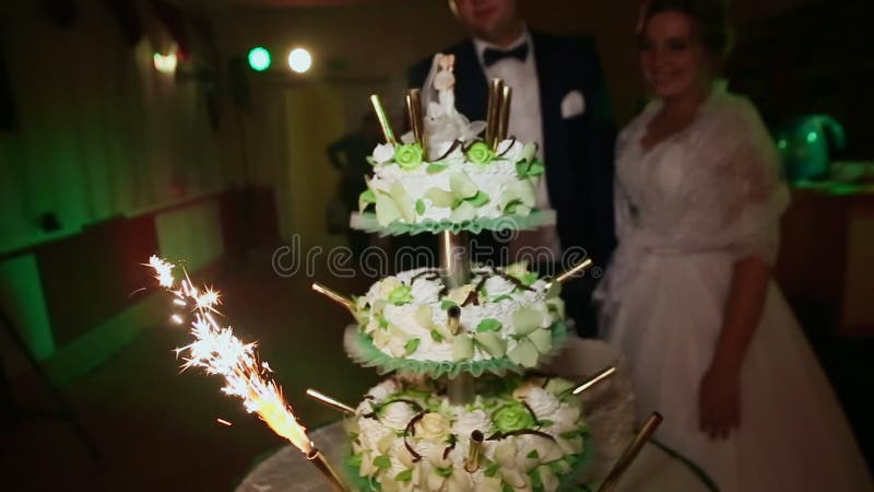 Les jeunes mariés au regard de mariage au gâteau avec brûler des lumières de Bengale
