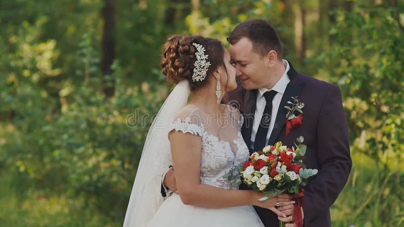 Les jeunes mariés avec un bouquet dans la forêt le marié étreignent sa jeune mariée Un baiser doux heureux ensemble Le moment du