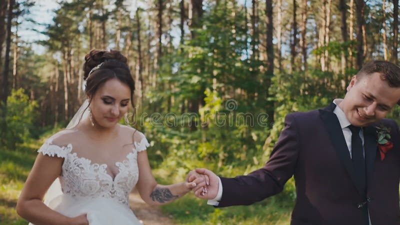 Les jeunes mariés marchant dans une forêt de pin, tenant des mains et regardant l'un l'autre Baiser d'air heureux ensemble Promen