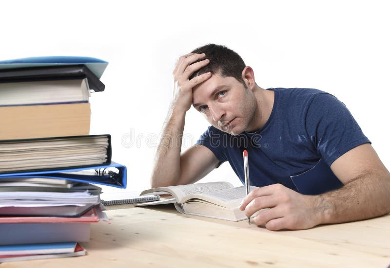 Young stressed Caucasian student studying pile of books on library desk preparing exam in stress feeling tired and overwhelmed in youth education concept. Young stressed Caucasian student studying pile of books on library desk preparing exam in stress feeling tired and overwhelmed in youth education concept