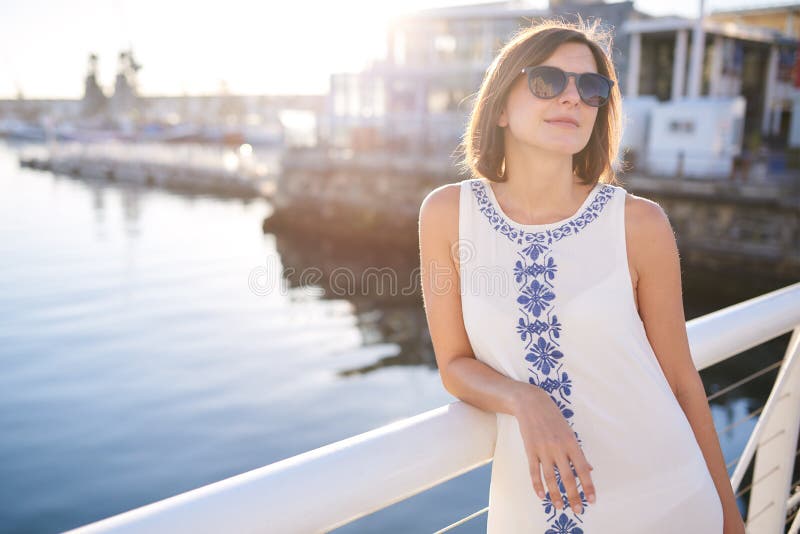 Les lunettes de soleil de port et l'été de femme s'habillent à côté de l'eau photographie stock Les lunettes de soleil de port et l'été de femme s'habillent à côté de l'eau photographie stock