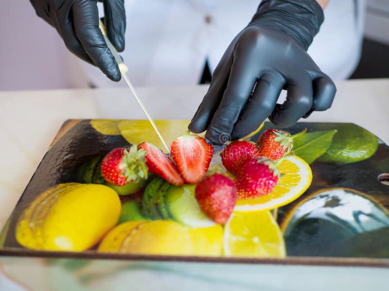 Les mains dans les gants en caoutchouc noirs ont coupé une fraise rouge mûre sur un tableau noir photos libres de droits Les mains dans les gants en caoutchouc noirs ont coupé une fraise rouge mûre sur un tableau noir photos libres de droits