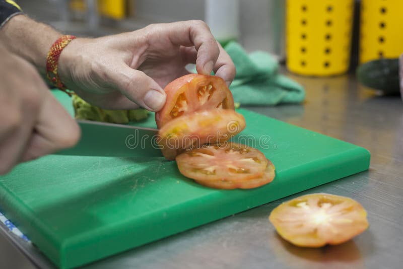Les mains de Chef coupant la tomate rose dans les tranches utilisant un couteau pointu photo libre de droits Les mains de Chef coupant la tomate rose dans les tranches utilisant un couteau pointu photo libre de droits