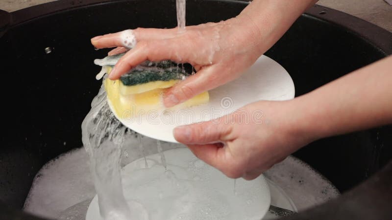 Les mains de femme lavent le plat à l'évier de cuisine, mouvement lent banque de vidéos