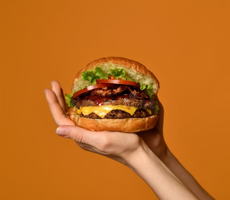 Les mains de femme tiennent le grand sandwich à hamburger de cheeseburger avec du boeuf et le lard de marbre sur le jaune images stock Les mains de femme tiennent le grand sandwich à hamburger de cheeseburger avec du boeuf et le lard de marbre sur le jaune images stock