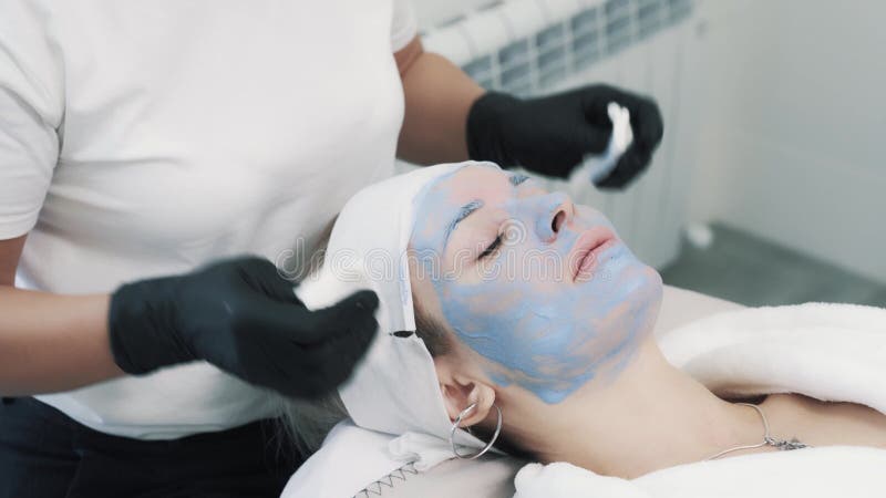 Les mains de l'esthéticienne efface le visage de la jeune femme superbe banque de vidéos