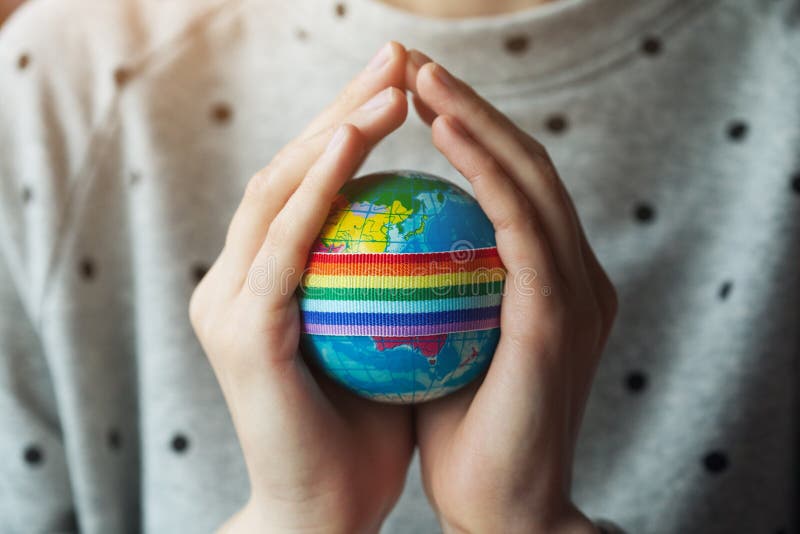 Les mains de la femme tenant le globe avec le ruban d'arc-en-ciel de LGBT image libre de droits Les mains de la femme tenant le globe avec le ruban d'arc-en-ciel de LGBT image libre de droits
