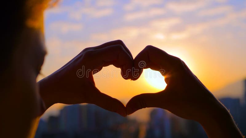 Les mains des femmes forment un signe en forme de coeur contre le coucher ou le lever du soleil banque de vidéos