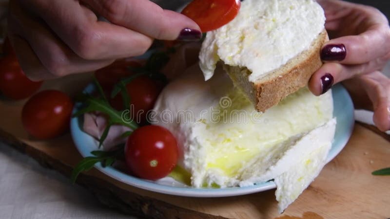 Les mains femelles mettent une tranche de tomates sur un morceau de mozzarella frais sur l'Italien de pain que le sandwich prêt à