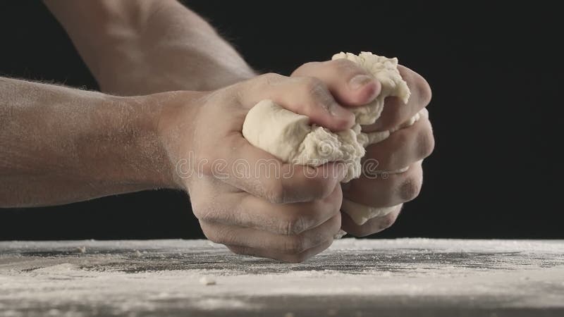 Les mains masculines pétrissent un morceau de pâte et la déchire en deux au-dessus de la table en bois saupoudrée de farine.