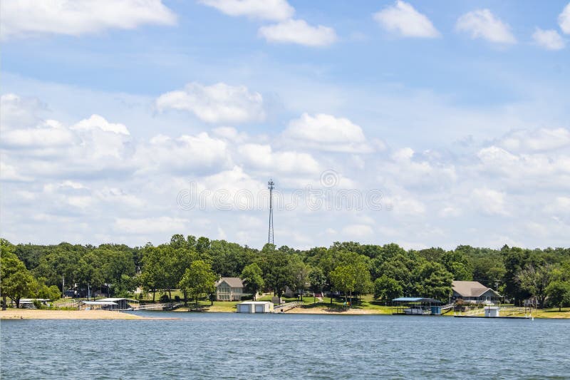 Les maisons de Lakeside et les docks de bateau avec des arbres et un émetteur dominent à l'arrière-plan sous un ciel bleu avec le image stock Les maisons de Lakeside et les docks de bateau avec des arbres et un émetteur dominent à l'arrière-plan sous un ciel bleu avec le image stock