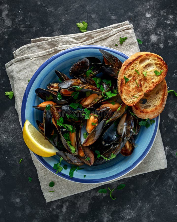 Les moules en beurre d'ail sauce servi avec le persil, le pain grillé et le citron image stock Les moules en beurre d'ail sauce servi avec le persil, le pain grillé et le citron image stock
