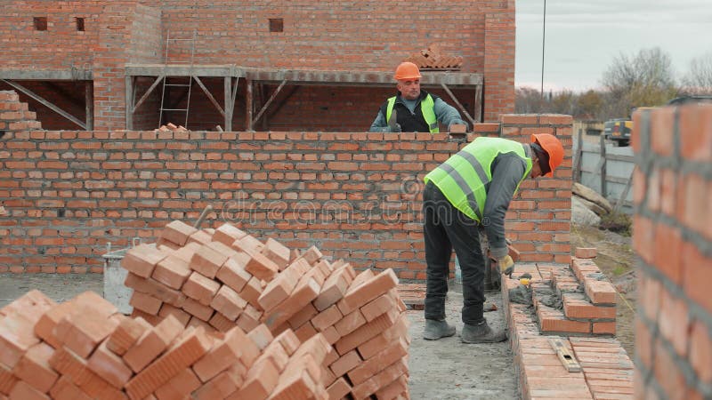 Les ouvriers du bâtiment mur de brique. Deux ouvriers du bâtiment en équipement de sécurité construisent un mur de brique dans une banque de vidéos