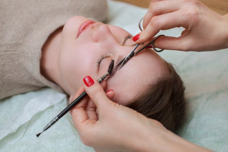 Les peignes d'artiste de maquillage et cisaillent ses fronts avec des ciseaux à une belle jeune fille images stock Les peignes d'artiste de maquillage et cisaillent ses fronts avec des ciseaux à une belle jeune fille images stock