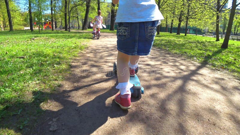 Les petites filles adorables montent en parc sur une bicyclette et un scooter clips vidéos