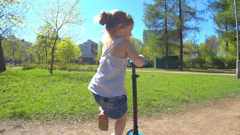 Les petites filles adorables montent en parc sur une bicyclette et un scooter clips vidéos