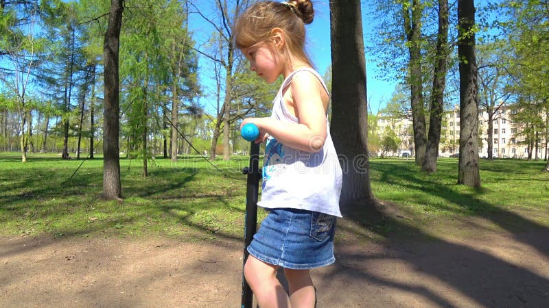 Les petites filles adorables montent en parc sur une bicyclette et un scooter banque de vidéos