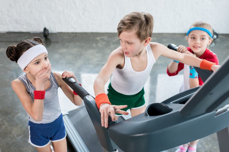 Les petits enfants dans les vêtements de sport s'exerçant sur le tapis roulant dans le gymnase, enfants folâtrent le concept d'éc images libres de droits Les petits enfants dans les vêtements de sport s'exerçant sur le tapis roulant dans le gymnase, enfants folâtrent le concept d'éc images libres de droits