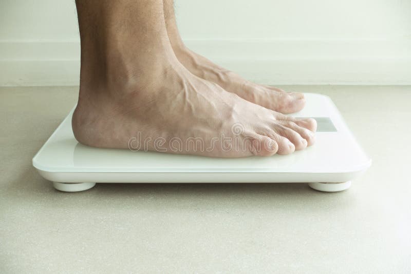 Les pieds de l'homme sur le poids vérifiant la machine photo libre de droits Les pieds de l'homme sur le poids vérifiant la machine photo libre de droits