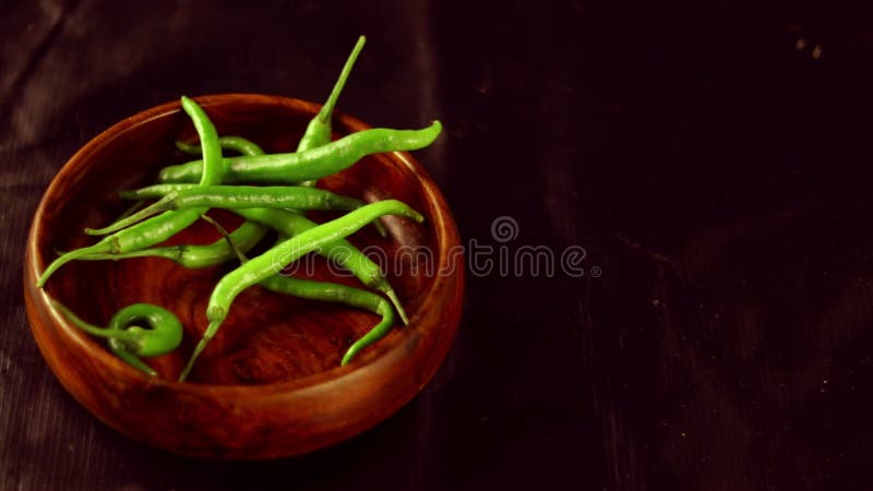 Les piments verts tombent dans le bol en bois de piment vert frais dans un bol en bois avec fond noir poivre vert ou piment banque de vidéos