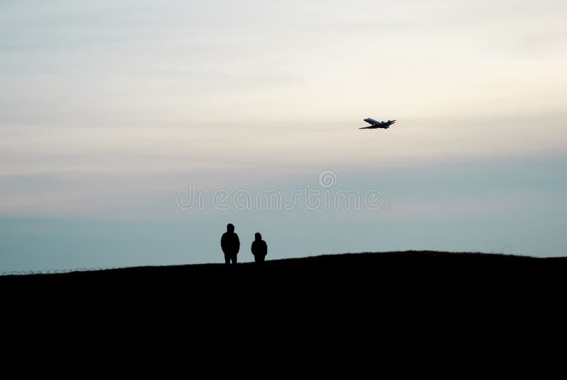 Les silhouettes du support de deux personnes sur une haute colline et observer une haute de vol d'avion dans le ciel photo libre de droits Les silhouettes du support de deux personnes sur une haute colline et observer une haute de vol d'avion dans le ciel photo libre de droits
